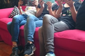 Mehrere Schülerinnen, die ein Buch nebeneinader lesen und dabei das Buch vor ihr Gesicht halten