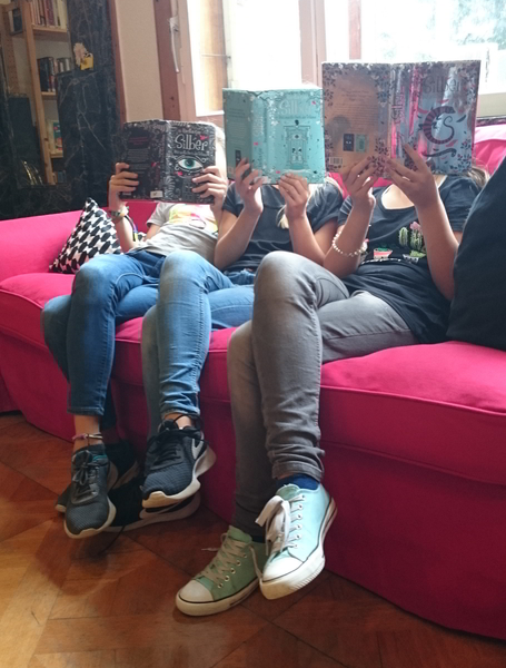 Mehrere Schülerinnen, die ein Buch nebeneinader lesen und dabei das Buch vor ihr Gesicht halten