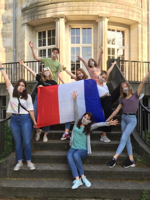 Verschiedene Schüler*innen mit einer Frankreich-Flagge, die ihre arme tri­um­phie­rend in die Höhe strecken